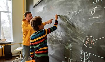 A teacher at a chalkboard working through math with a student